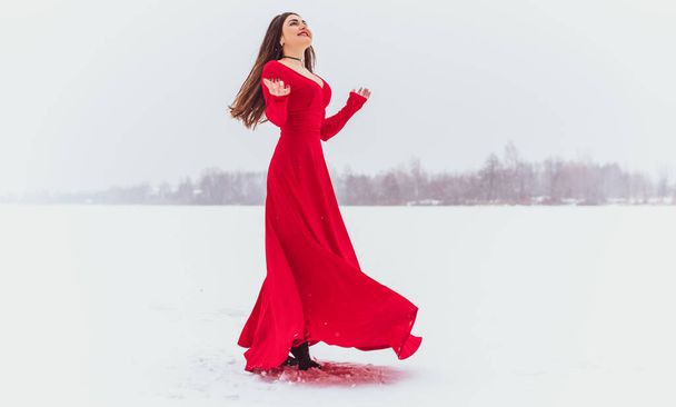 Mujer hispana bailando en vestido de seda en el día nevado, vestido rojo artístico ondeando y agitando tela, concepto de pasión - Foto, imagen