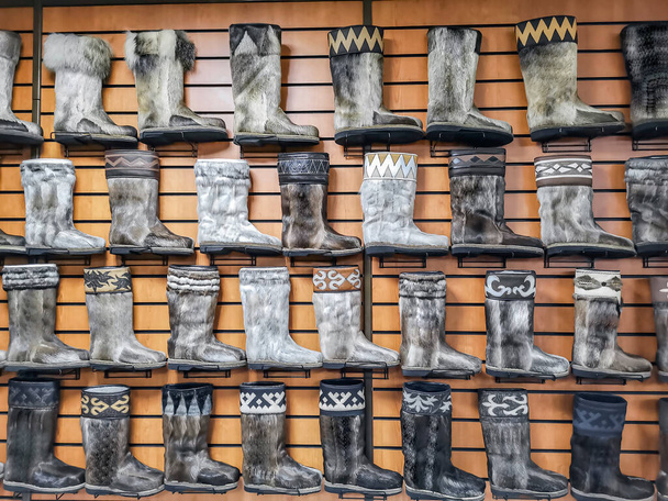Piel unty o llantas, o botas ugg siberianas - en una exposición y venta en Irkutsk. Una variedad de zapatos tradicionales de invierno de piel en Siberia y el norte de Rusia. Botas altas de venado, alce, wapiti y piel de foca adornada con adornos de cuero.  - Foto, imagen