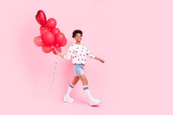 Полноразмерный профиль боковой фотографии молодой жизнерадостной женщины, гуляющей с многочисленными воздушными шарами, изолированными на розовом фоне - Фото, изображение