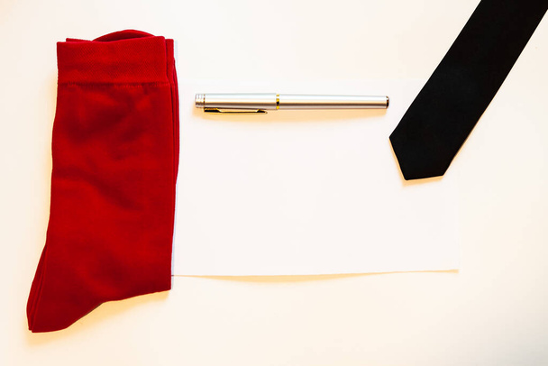 Κόκκινες κάλτσες με μαύρη γραβάτα και στυλό σε χάρτινο φόντο με θέση για κείμενο - Φωτογραφία, εικόνα