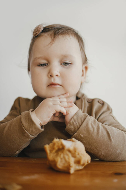 Sevimli bebek, modern İskandinav odasındaki ahşap masada zencefilli kurabiye hamuru yoğurmak için annesine yardım ediyor. Küçük tatlı kız Noel kurabiyeleri yapmaya yardım ediyor. Otantik komik an - Fotoğraf, Görsel