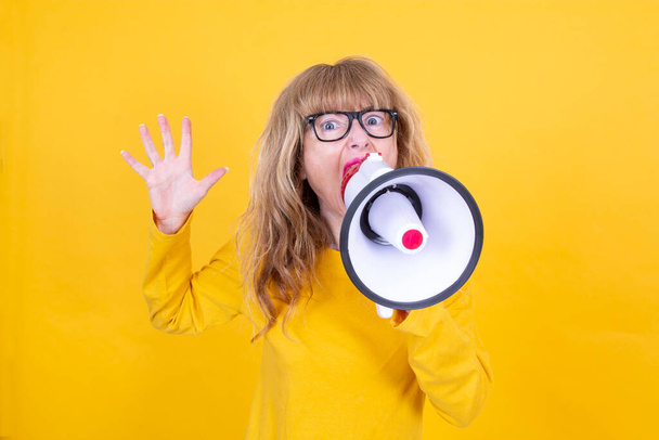 mature woman yelling with megaphone with yellow background - Photo, Image