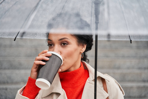 Lady walking with cup of coffee on autumn street under the umbrella - Valokuva, kuva