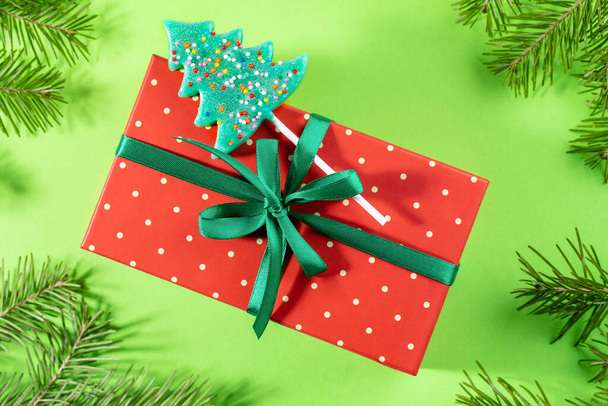Red in polka dots wrapped box decorated with green ribbon, bow and lollipop as Xmas tree on green. - Valokuva, kuva