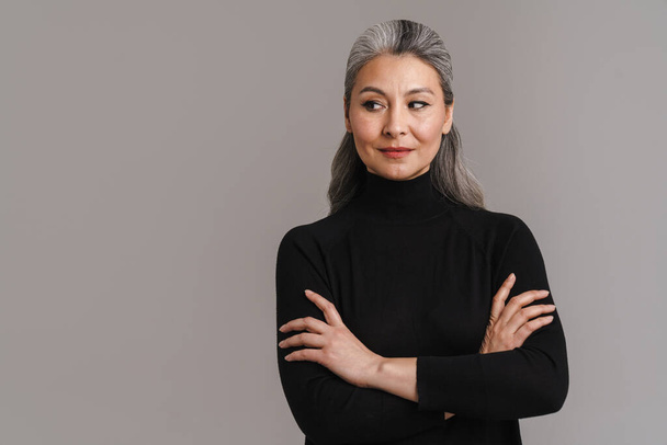 Mature asian white-haired woman posing with her arms crossed isolated over grey background - Zdjęcie, obraz