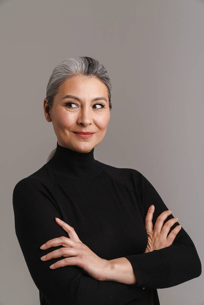 Mature white-haired woman smiling while posing with her arms crossed isolated over grey background - Photo, Image