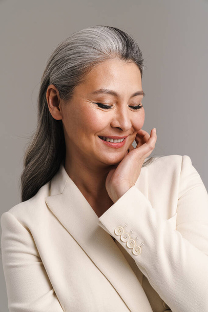 Mature woman with white hair smiling and posing at camera isolated over grey background - Foto, Imagen