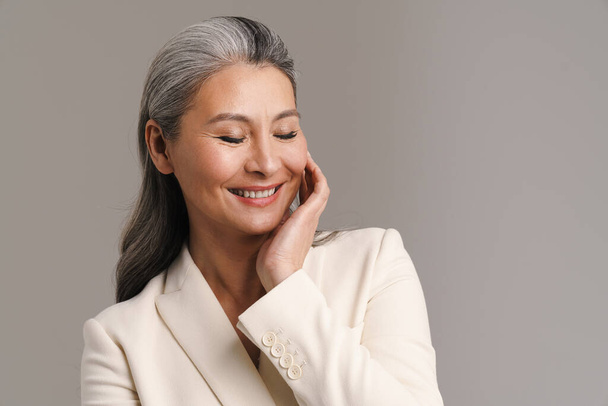 Mature woman with white hair smiling and posing at camera isolated over grey background - Valokuva, kuva