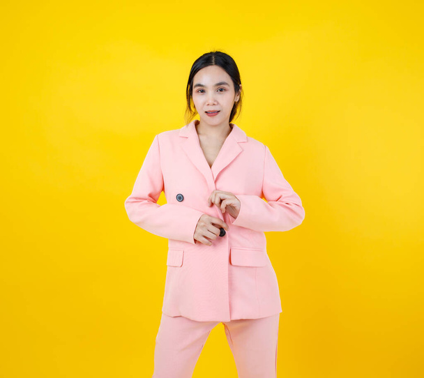 Мила і сексуальна азіатська дівчина прикріпляє до себе кнопку чудової рожевої ділової куртки і з упевненістю посміхається, що вона виставляє дивовижний одяг для сучасної робочої моди і способу життя. Привабливий одяг для дорослих.. - Фото, зображення