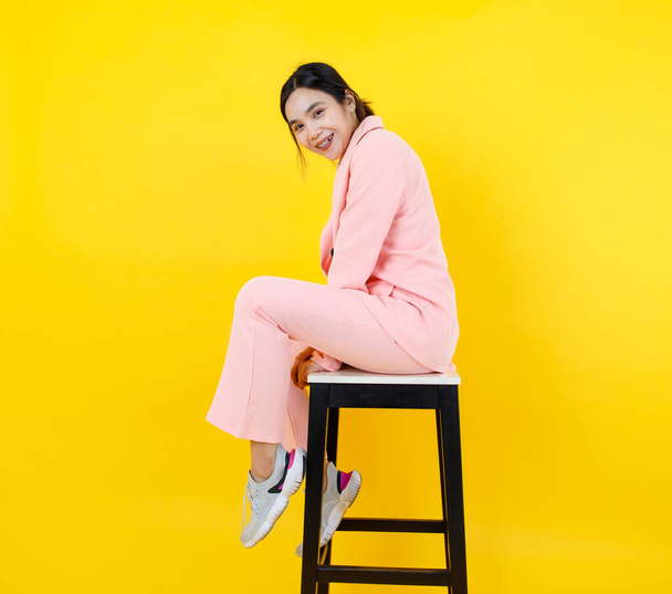 Naughty Asian girl on pink pastel jacket and pants sit leisurely on high chair posing model character for adult costume fashion. Relaxing portrait for modern clothing and suit for female outfit. - Photo, Image