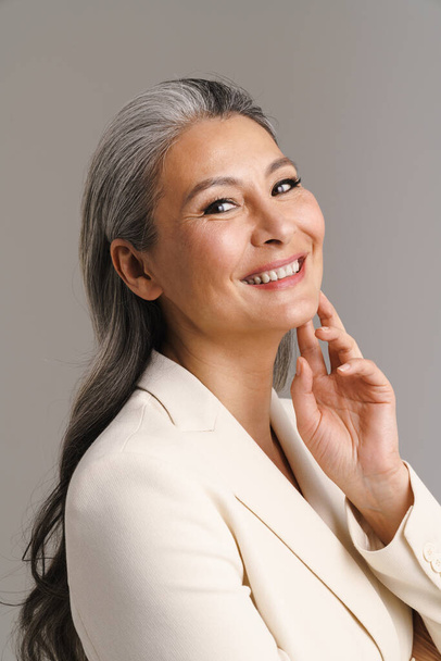 Mature woman with white hair smiling and looking at camera isolated over grey background - Foto, Bild