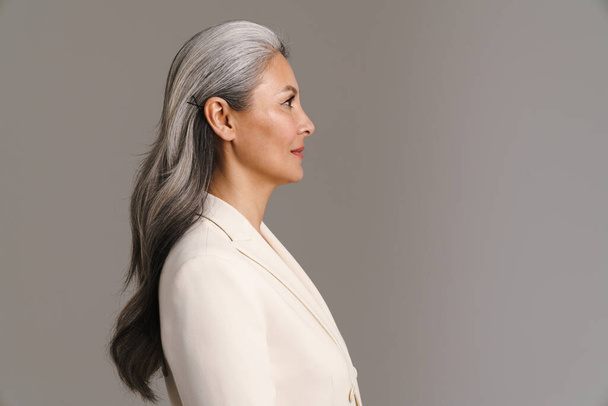 Mature asian woman with white hair posing in profile isolated over grey background - Fotografie, Obrázek