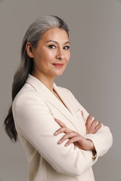 Mature asian white-haired woman posing with her arms crossed isolated over grey background - Fotoğraf, Görsel