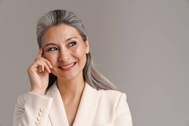 Mature woman with white hair smiling and looking aside isolated over grey background - Фото, зображення
