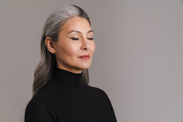 Mature asian white woman posing with her eyes closed isolated over grey background - Foto, Imagen
