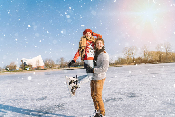 Loving couple in warm sweaters having fun on ice. Woman and man ice skating outdoors in sunny snowy day. Active date on ice arena in winter Christmas Eve. Romantic activities and lifestyle concept. - Photo, Image
