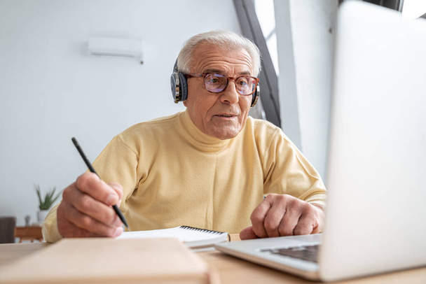 Concentrated older grandfather watching online webinar and writing notes - 写真・画像