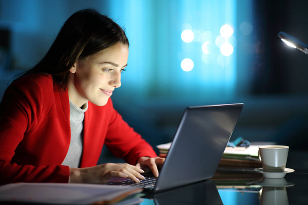 Happy businesswoman in red working using laptop on a desk in the night at home - Foto, imagen