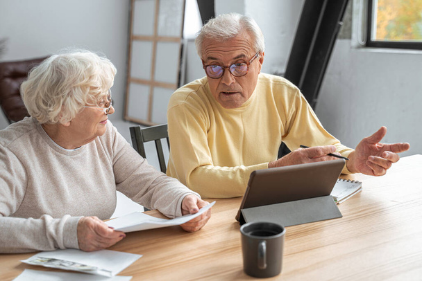 Worried senior couple checking bills using tablet computer - Foto, immagini