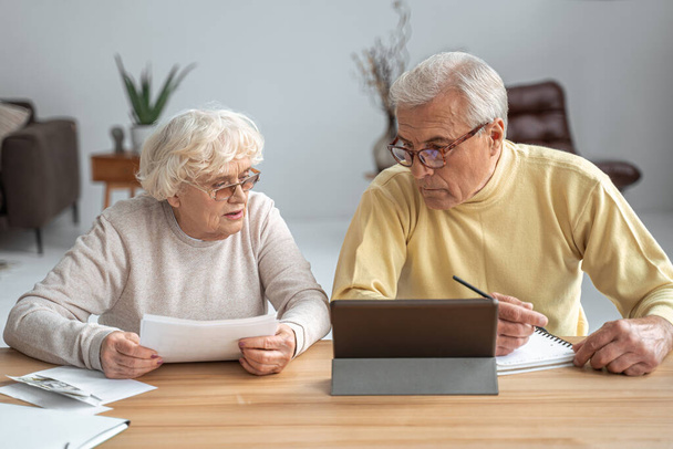 Husband and wife sitting at the table in living room and managing household document pay - Foto, afbeelding