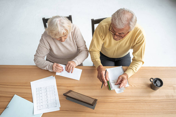 Retirement couple checking accountancy and bills while looking at each other - Foto, afbeelding