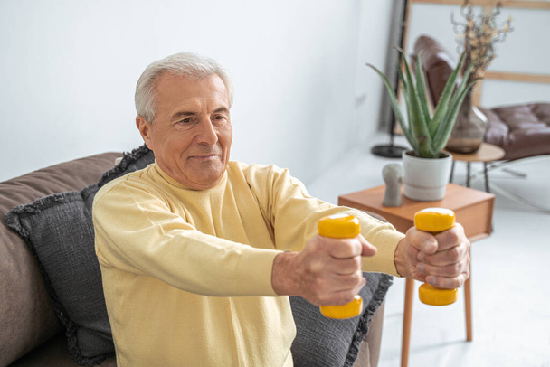 Senior man exercising at home while sitting on the couch - Photo, image