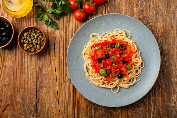 Italian spaghetti alla Pultanesca with tomatoes and olives. Served without meat and cheese. Top view. Natural wooden background.  - Foto, Bild