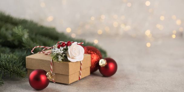  Christmas gift box on a background of Christmas tree branches, red Christmas balls and Christmas lights. Copy space. - 写真・画像