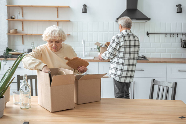 Happy elderly couple unpacking carton boxes in their new house - Foto, Imagem
