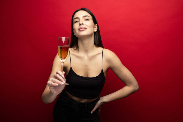 Schöne Brünette mit einem Glas Champagner auf rotem Hintergrund - Foto, Bild