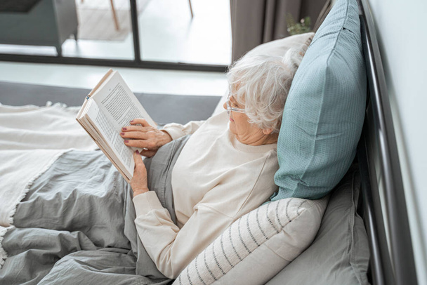 Cute retirement woman is reading in bedroom - Photo, Image