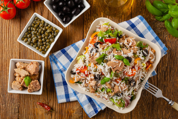 Italian tuna salad with rice, olives and capers. Top view. Natural wooden background. - Foto, Imagem