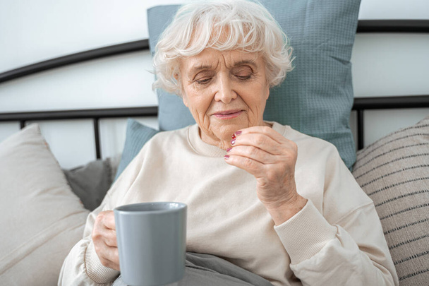 Senior female eating vitamins and drinking water during the morning - Foto, imagen