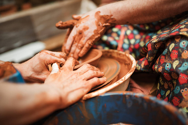 un alfarero y un estudiante esculpen platos en una rueda de alfarero hecha de arcilla - Foto, Imagen