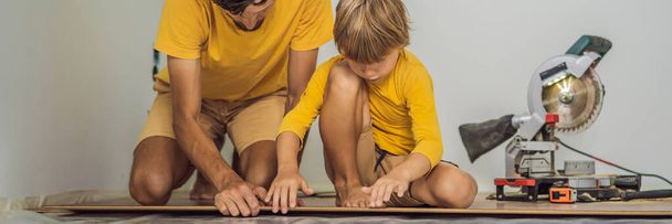BANNER, LONG FORMAT Father and son installing new wooden laminate flooring on a warm film floor. Infrared floor heating system under laminate floor - Фото, изображение