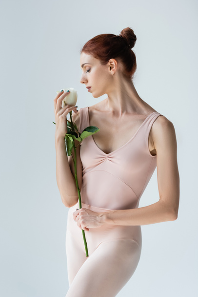 redhead ballerina with closed eyes smelling rose isolated on grey - Photo, Image