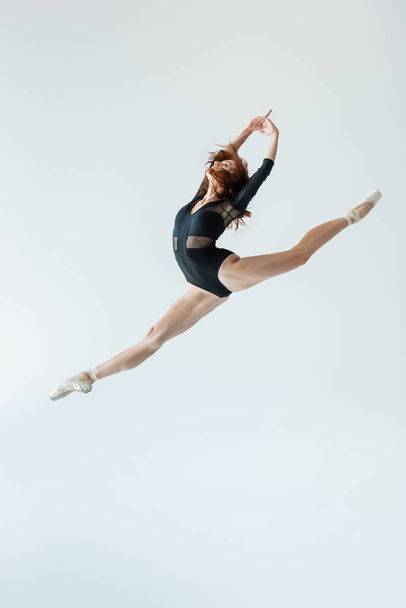 full length of ballerina in black bodysuit jumping isolated on grey - Foto, afbeelding