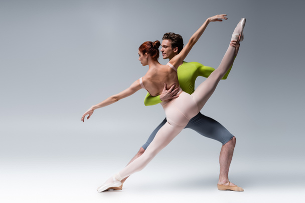 full length of man and flexible woman performing ballet dance on grey - Fotoğraf, Görsel