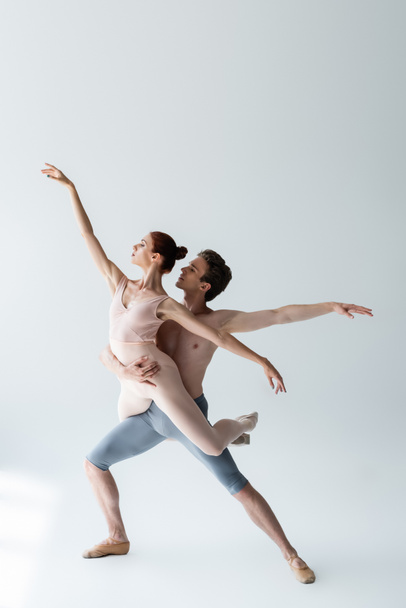 full length of shirtless man and flexible woman in bodysuit performing ballet dance on grey - 写真・画像