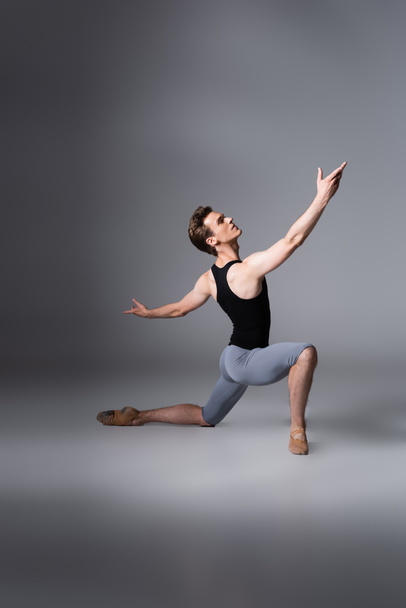 young ballet dancer in black tank top performing ballet dance while standing on knee on dark grey  - Photo, Image