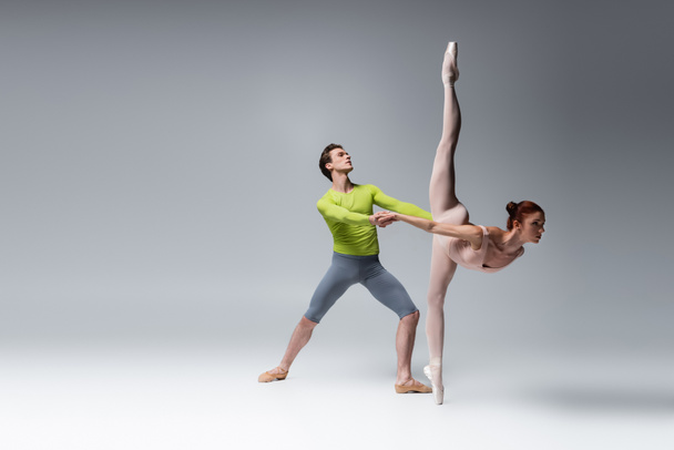full length of ballet dancer supporting ballerina during dance on dark grey - Foto, immagini