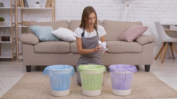 Концепция охраны окружающей среды. Молодая веселая домохозяйка в фартуке складывает бумажные отходы в фиолетовый мусорный бак для переработки - Кадры, видео