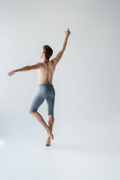 young shirtless ballet dancer with raised hand on grey  - Фото, изображение