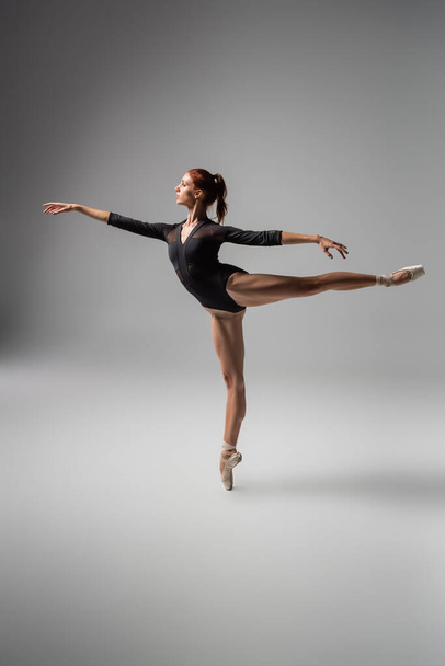 full length of pretty woman in ballet shoes performing ballet dance while standing on pointe shoe on dark grey - Zdjęcie, obraz