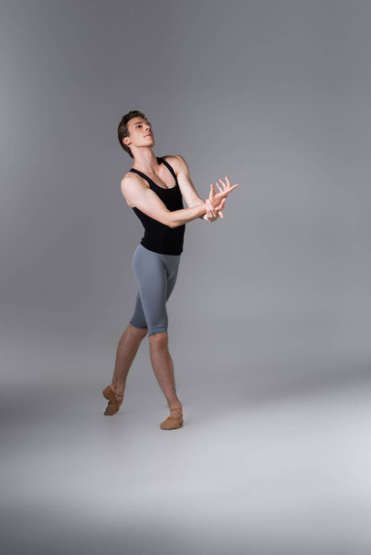 longitud completa de elegante bailarina de ballet haciendo gestos mientras realiza danza de ballet en gris oscuro  - Foto, Imagen