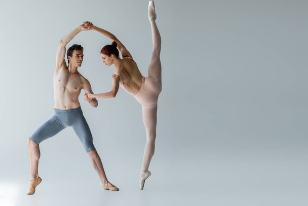 full length of young cheerful ballet dancer performing ballet dance with ballerina on grey  - Fotó, kép