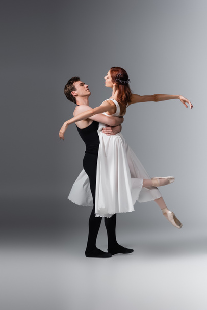tutta la lunghezza dell'uomo sollevando graziosa ballerina in abito bianco su grigio scuro - Foto, immagini