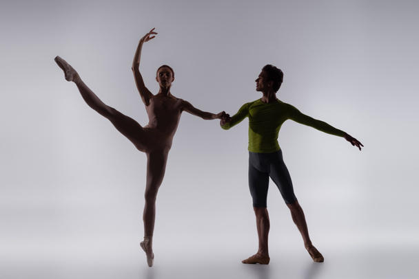 silhouette of dancer holding hands with ballerina on grey - Foto, immagini