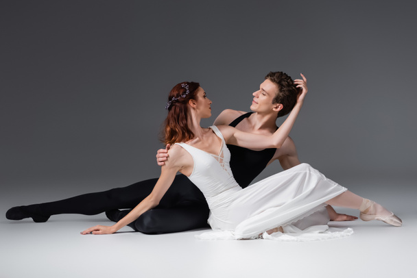 graceful ballerina in white dress dancing with partner on dark grey - Fotografie, Obrázek