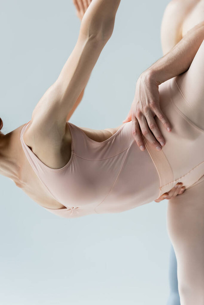partial view of flexible ballerina dancing ballet with partner isolated on gray - Fotó, kép